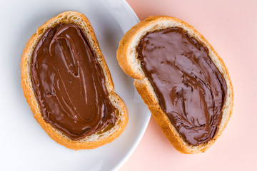 Pieces of long loaf with chocolate, nut paste on a plate. Nut chocolate cream sandwiches on a breakfast. Top view