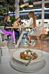Girlfriends eat at the cafe. Fresh juices and salads on the table. Concept: a healthy lifestyle. Cozy restaurant with yellow light and green background.