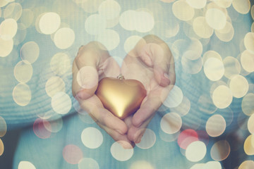 Woman hands are holding a beautiful glossy gold heart in a snow winter background. Love and St. Valentine cozy concept.