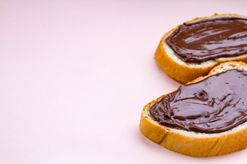 Pieces of loaf with chocolate paste on a pink background. Chocolate sandwiches with nut paste on a breakfast. Copy space