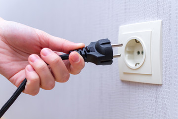 Ready to connect. Plugging electrical, black plug in electric socket on wall. - obrazy, fototapety, plakaty