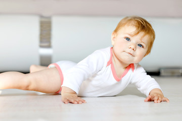 Naklejka premium Little cute baby girl learning to crawl. Healthy child crawling in kids room. Smiling happy healthy toddler girl. Cute toddler discovering home and learning different skills