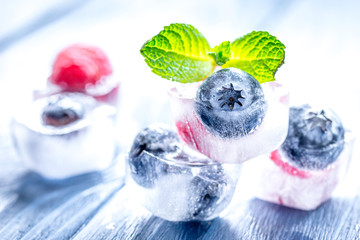 Berries frozen in ice cubes with mint on wooden table background
