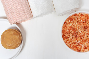 Spa accessories - white towels, round soap, aroma sea salt. Items for bathroom on white background with copy space. Top view.