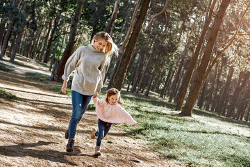 Happy, stylish little curly girl is running with her beautiful mother in forest