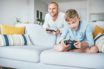 Obraz premium Father watching his son playing TV video game using the gamepad in the living room. Modern game devices concept.