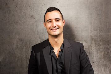 Close up smiling man posing against gray wall with black blazer