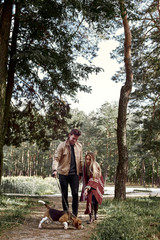 Young couple are walking with dog in forest