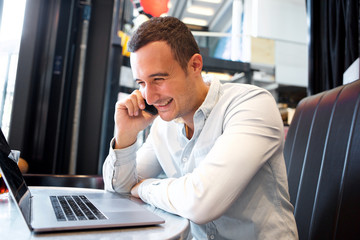 Close up happy man sitting at cafe with laptop and talking on mobile phone