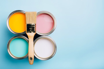 Brush with wooden handle on open cans on blue pastel background. Yellow, white, pink, turquoise colors. Renovation concept. Place for text.