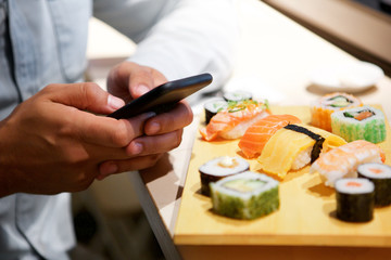 Close up hands with smart phone at sushi bar © mimagephotos