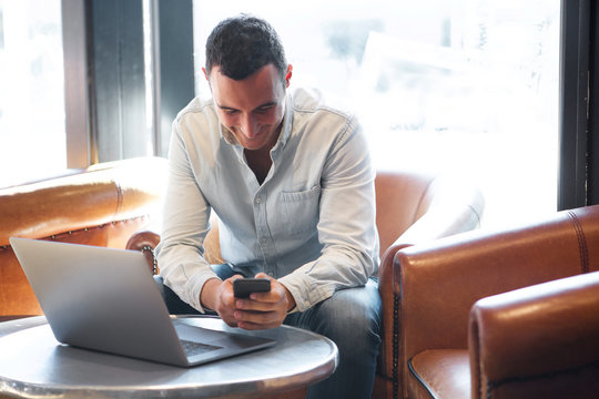 man sitting at cafe with mobile phone and laptop computer