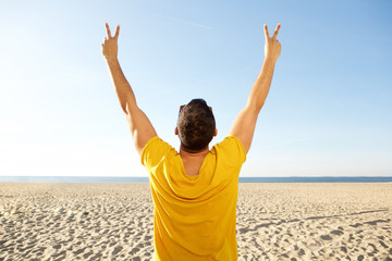 back of man cheering with hands raised at the beach