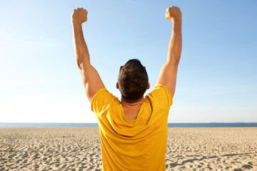 back of man cheering with arms raised at the beach