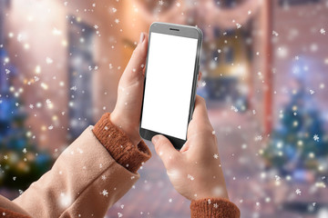 Female hands use phone with empty screen on snow-covered street while snowing. Mockup