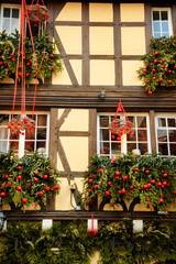 Fototapeta na wymiar Christmas decoration with christmas wreaths and red apples on house facade in medieval city of Strasbourg (France) which is considered as a Capital of Noel.
