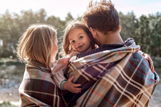 Young parents hugg their little daughter in autumn forest near the lake.