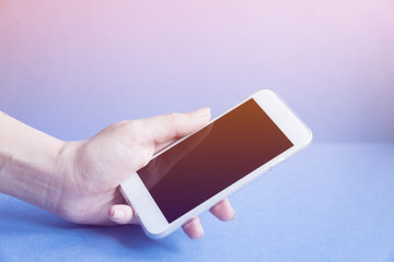 white modern mobile phone in female's hand on blue background, toned