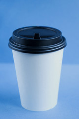 white paper kraft disposable cup for coffee with black plastic lid. coffe to go on blue background.