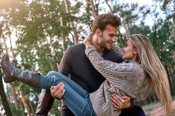 Fototapeta premium Young man holding his girlfriend on hands in autumn forest.