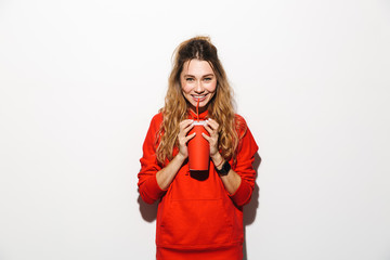Fototapeta premium Image of attractive woman 20s wearing red sweatshirt drinking soda from paper cup using straw, isolated over white background