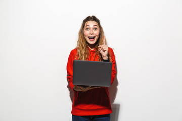 Obraz premium Image of charming woman 20s wearing red sweatshirt holding laptop, isolated over white background