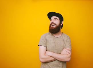 Portrait of cheerful bearded man smiling and looking away over yellow background