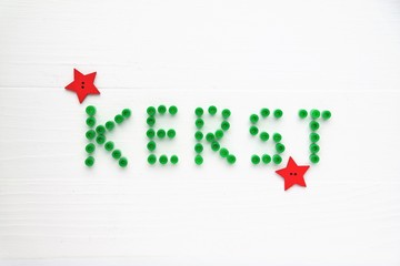 Christmas card in Dutch language. Decorative green letters and red stars. White wooden background, top-view perspective and text space. 
