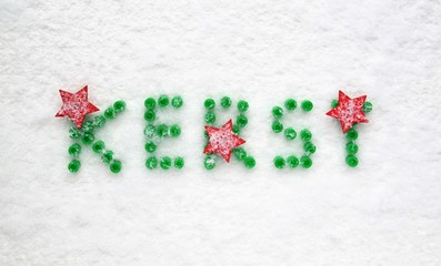 Christmas card in Dutch language. Decorative string beads, green letters and red stars. White snowy background, top-view perspective and text space
