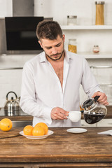 handsome man in shirt pouring coffee into cup in morning at kitchen