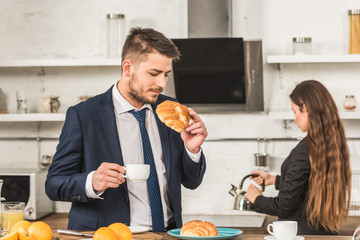 boyfriend having breakfast and girlfriend putting kettle on stove at home, social roles concept
