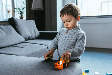 cute boy playing with toy cars in living room at home