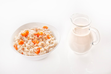 Oatmeal with pumpkin and nuts in a plate and a glass jug with milk on a white background. Close-up. Copy space