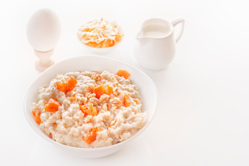 Oatmeal with pumpkin and nuts in a plate, vegetable salads, a boiled egg and a jug with milk on a white background. Close-up. Copy space