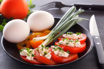Sliced tomatoes with cheese and herbs in a black plate with onions, sweet peppers and eggs. Close-up