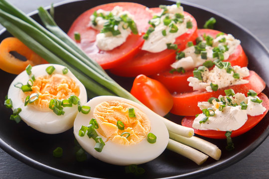 Half boiled eggs with tomatoes, green onions, sprinkled with greens in a black plate on a gray wooden table. Close-up