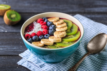 Healthy breakfast with delicious acai smoothie in bowl on dark background