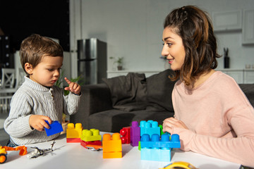 Obraz na płótnie Canvas little boy and his mother playing with colorful plastic blocks at home