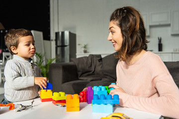 happy mother and little son playing with colorful plastic blocks at home
