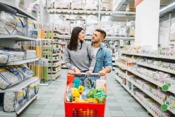 Young woman with cart full of goods in supermarket