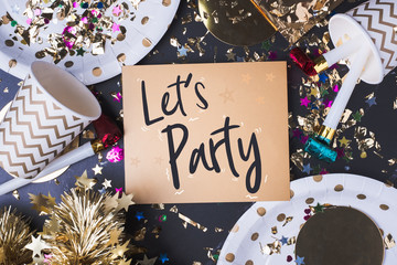 Let's party brush stroke handwriting on golden greeting card with party cup,party blower,tinsel,confetti.Holiday celebrate party time.top view tabletop.