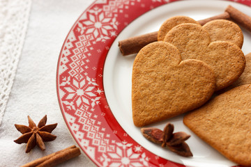 Gingerbread heart-shaped cookies with cinnamon sticks and anise stars on a red plate