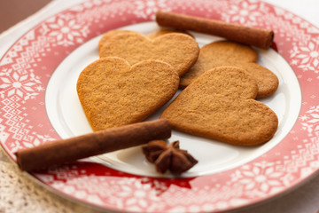 Gingerbread heart-shaped cookies with cinnamon sticks and anise stars on a red plate