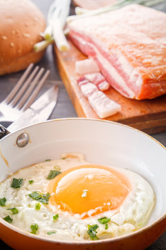 Fried egg in a pan, bacon, bread and green onions are cooked for breakfast on a wooden gray table. Close-up