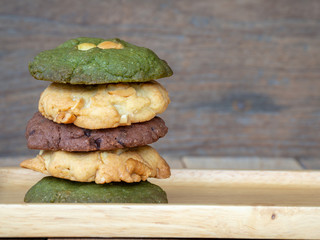 Multiple color cookies inclusive peanut butter, green tea cookies, and Chocolate Chip Cookies. Overlaid by alternating colors on wood plate. - Powered by Adobe