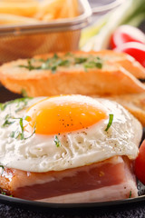 Fried egg with bacon with fried pieces of bread, greens and tomatoes. Close-up.