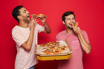 Handsome happy young men friends isolated over red wall background holding big pizza.