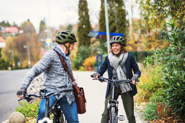 Active senior couple with electrobikes standing outdoors on pathway in town.