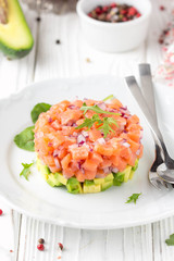 Salmon tartare with red onion, avocado, arugula, bread toast. Beautiful snack, dietary food, appetizer for Christmas holiday. On white wooden background