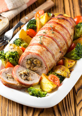Pork roll wrapped in bacon stuffed with mushrooms and beans, vegetables on the side. Beautiful festive main dish for Christmas holidays